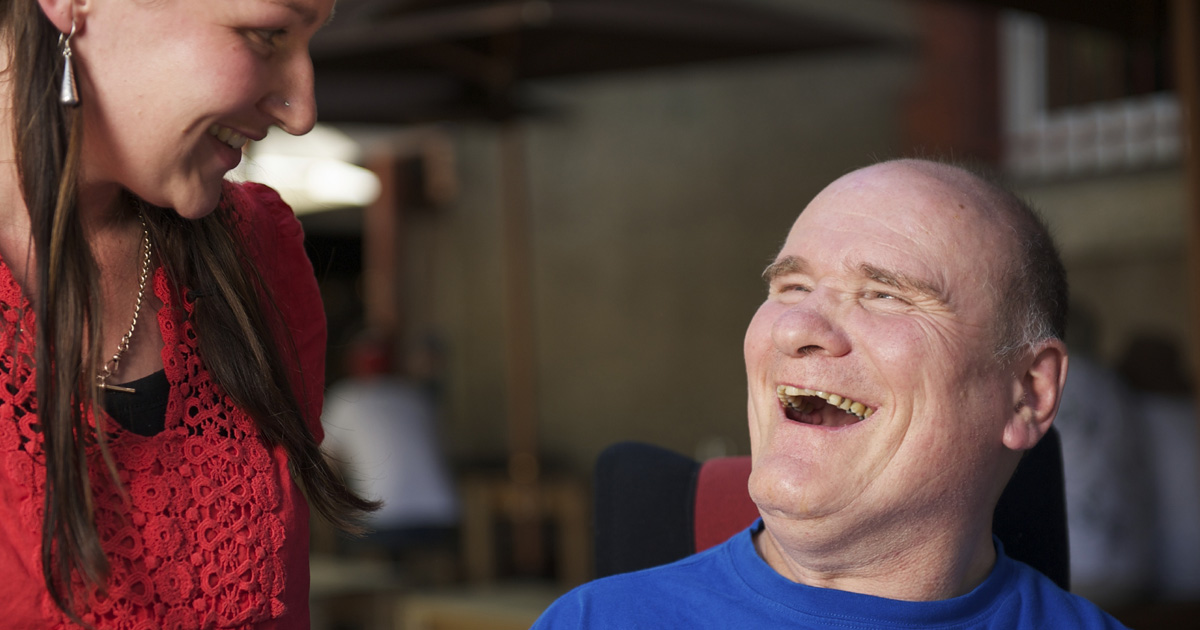 An older man with intellectual disability laughing with his support person